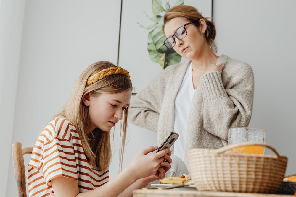 teenage girl on her phone, worried looking parent