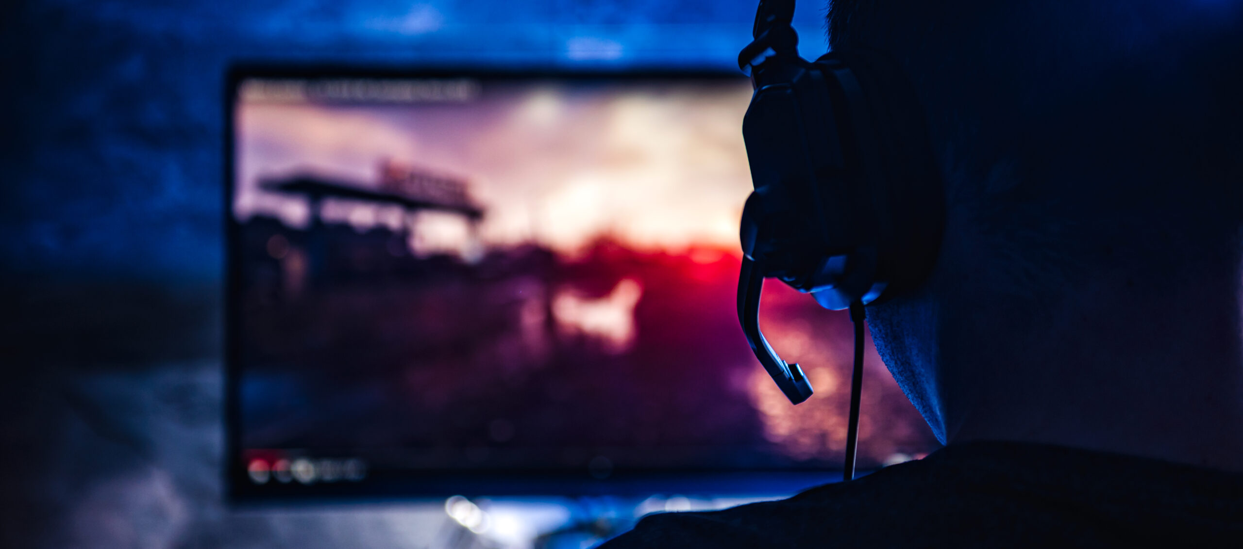 picture of a boy gaming with his headset on and a monitor