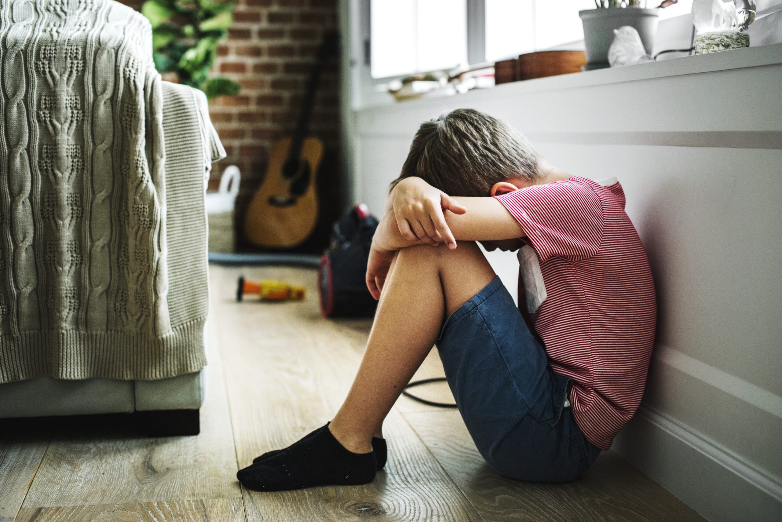 Young boy sat on he floor with his head in his arms